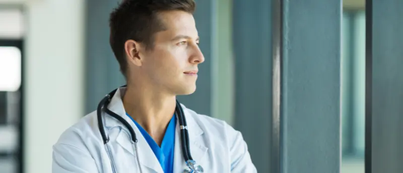 Médico jovem pensando sobre a importância de se ter um site para médicos e divulgar o seu trabalho na internet